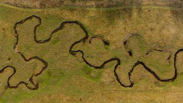 Aerial view of a serpentine stream meandering through a landscape of contrasting greens and browns, creating a captivating natural tapestry, Bjelasnica, Bosnia and Herzegovina.