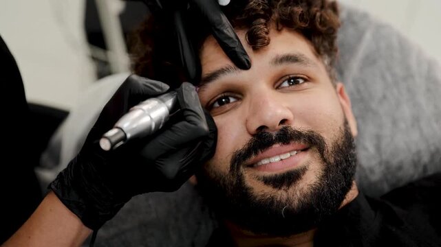 Happy man undergoing cosmetic eyebrow microblading procedure at a beauty salon