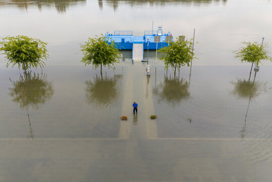 Aerial view of the blue ferry terminal at the river's edge, partially submerged under floodwaters, with a lone figure standing on the walkway, Batina, Osijek-Baranja County, Croatia.