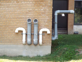 A section of the exterior brick wall of a building with several visible pipes and vents, likely part of the mechanical system.