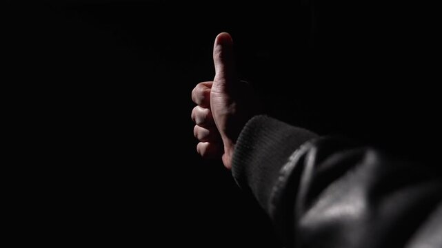 POV, close-up first person view of a man's hand showing a thumbs up gesture on a black background.