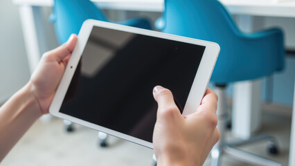 Person holds tablet device with blank screen, showcasing modern technology bright, minimalistic environment. blue chairs background add pop