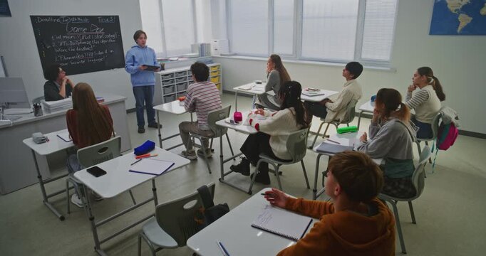 Boy in Blue Hoodie Presents Report on Educational Project For Game Development to Classmates and Teacher. Pupils Listen Intently. Concept Public Speaking Skills, Project Based Learning. Dolly Shot.