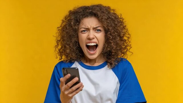 A woman with curly hair is yelling at her phone against a yellow background