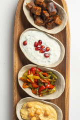 Set of traditional Mediterranean appetizers in small bowls with eggplant, peppers, hummus, and yogurt sauce
