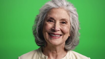 Closeup portrait of a happy senior woman with gray hair smiling broadly and looking directly at the camera against a vibrant green screen background expressing joy and positive emotions. - Powered by Adobe