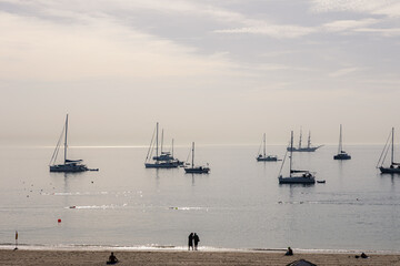 Tranquil morning seascape in Cascais, Portugal with sailboats and catamarans anchored near shore under soft light and a hazy sky