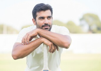 Cricket sport Handsome sportsman poses with bat on cricket field wearing white, relaxed, thoughtful, resting arms on willow equipment outdoors