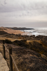 Overcast coastal view near Boca do Inferno, Portugal with rugged cliffs, sandy beach, and waves breaking along the Atlantic shore
