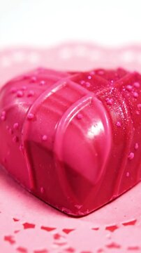 A visually captivating, close-up shot of a vibrant heart-shaped confectionery, likely a chocolate or candy, presented in a rich pink hue. The surface of the sweet treat is intricately textured and ado