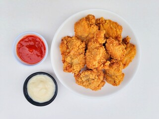 Crispy and crunchy fried chicken in a white plate and mayonnaise sauce in a small black bowl and chili sauce in a small white bowl on a white background.