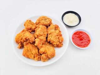 Crispy and crunchy fried chicken in a white plate and mayonnaise sauce in a small black bowl and chili sauce in a small white bowl on a white background.