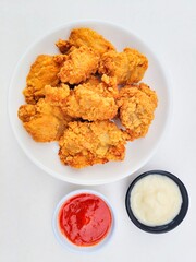 Crispy and crunchy fried chicken in a white plate and mayonnaise sauce in a small black bowl and chili sauce in a small white bowl on a white background.