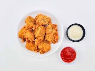 Crispy and crunchy fried chicken in a white plate and mayonnaise sauce in a small black bowl and chili sauce in a small white bowl on a white background.