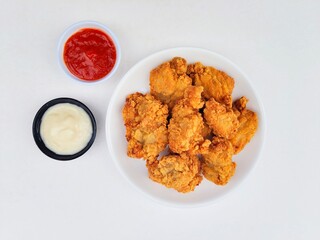 Crispy and crunchy fried chicken in a white plate and mayonnaise sauce in a small black bowl and chili sauce in a small white bowl on a white background.
