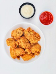 Crispy and crunchy fried chicken in a white plate and mayonnaise sauce in a small black bowl and chili sauce in a small white bowl on a white background.