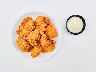 Crispy and crunchy fried chicken in a white plate and mayonnaise sauce in a small black bowl on a white background.