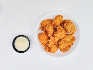 Crispy and crunchy fried chicken in a white plate and mayonnaise sauce in a small black bowl on a white background.