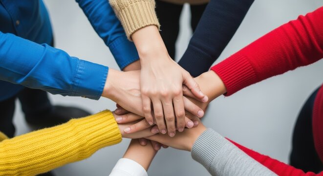 A group of people in colorful sweaters unite, hands joined in a symbol of teamwork and shared purpose. The image conveys a sense of collaboration and support.