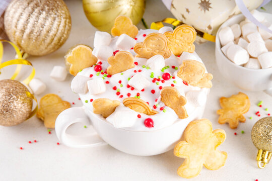 Festive tasty Christmas hot chocolate with whipped cream, marshmallows, sugar sprinkles, Christmas symbol biscuits, sugar cookies in form of gingerbread men, on festive holiday decorated background - Powered by Adobe