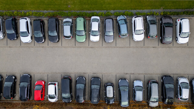 Aerial view showcases neatly aligned cars in a parking lot with diverse vehicle colors and sizes.