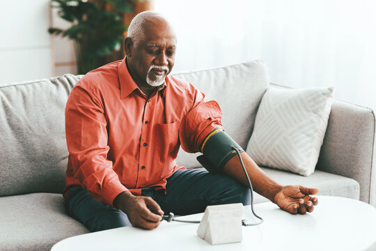 An elderly man sits on a sofa, monitoring his blood pressure using a digital device. The setting is cozy, with soft lighting and a relaxed atmosphere.