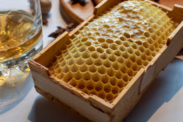 Detailed macro shot of natural yellow honeycomb in a wooden box with blurred elements of premium whiskey. Texture of natural bee cells filled with honey