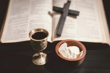 Holy communion bread and wine cup placed on the Holy Bible, symbolizing the Lord Supper, Eucharist, sacrifice of Jesus Christ, Christian worship and remembrance of faith.