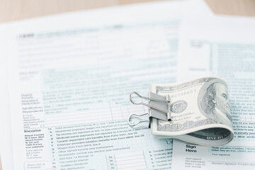 Concept of tax season and financial accounting. Stack of US dollar bills clipped on income tax forms, symbolizing payment, business finance, budget management and personal income report.