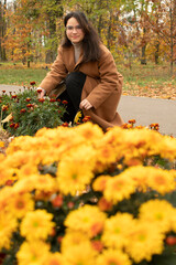 Woman in brown coat plucks marigolds from flowerbed in autumn park	