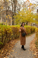 Woman in brown coat standing an alley in an autumn park	