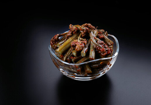 A glass cup with bracken fern salad stands against a beautiful black background.