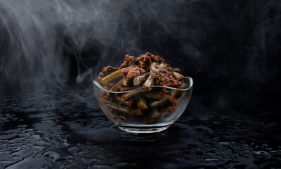 Bracken fern salad stands on a beautiful wet surface. Side view. Smoke above a bowl of fern salad.