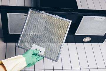 Naklejka premium Woman's hand removing a filter from cooker hood for cleaning or service. Replacing filter in kitchen hood. Professional cleaning kitchen hood with rag