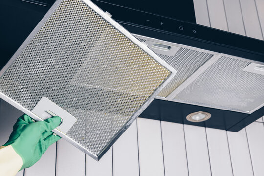 Woman's hand removing a filter from cooker hood for cleaning or service. Replacing filter in kitchen hood. Professional cleaning kitchen hood with rag