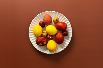 A collection of brightly colored Easter eggs in various sizes and patterns is displayed on a white scalloped plate, resting on a warm brown surface