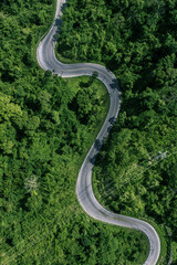 Aerial top view of a winding road cutting through lush green tropical forest. Scenic mountain highway surrounded by dense jungle trees, showing the beauty of nature and travel adventure concept.
