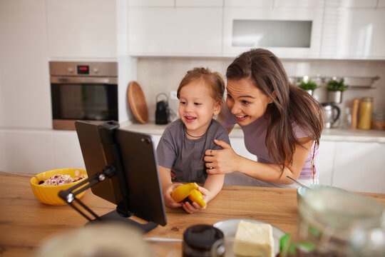 Joyful family moment in the kitchen with a child and parent watching a screen, sharing snacks, and smiling together during a relaxing afternoon.