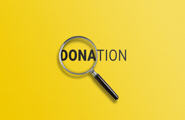 A magnifying glass focuses on DONATION against a yellow background 