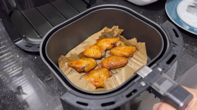 Opening air fryer with roasted BBQ chicken wings inside, hand pulling the drawer