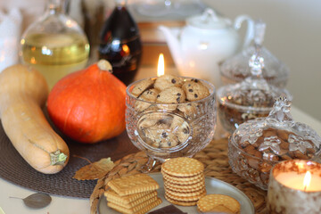 Lit candles, cookies, chocolate, nuts, tea, wine, pumpkins, books, reading glasses and autumn leaves on the table. Autumnal hygge at home. Selective focus.