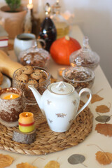 Lit candles, cookies, chocolate, nuts, tea, wine, pumpkins, books, reading glasses and autumn leaves on the table. Autumnal hygge at home. Selective focus.