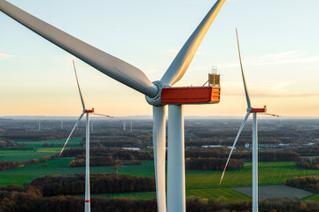 Close-up of modern wind turbines in a rural landscape at sunset. The blades rotate in warm evening light above green fields, symbolizing renewable energy and sustainability.