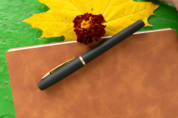 Pen, brown-covered notebook, marigold and yellow maple leaf