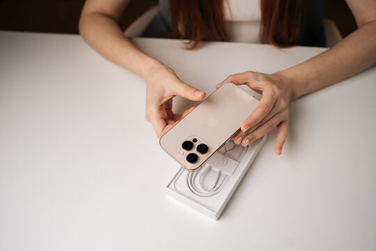 Ufa, Russia - 17 August 2025. Female hands unboxing gold iPhone 16 pro, revealing sleek device on white table, highlighting premium smartphone design. Concept of anticipation and excitement.