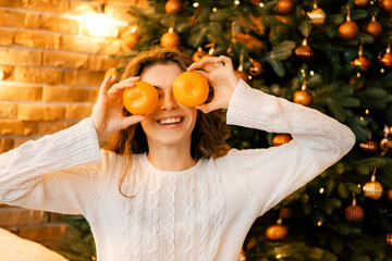 beautiful curly girl in a white sweater with dark hair smiling and holding tangerines. happy new year portrait