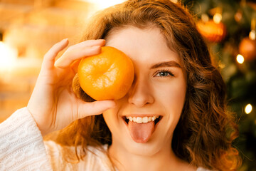 beautiful curly girl in a white sweater with dark hair smiling and holding tangerines. happy new year portrait