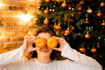 beautiful curly girl in a white sweater with dark hair smiling and holding tangerines. happy new year portrait