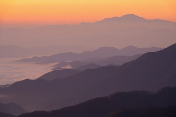 Fototapeta premium Serene mountain landscape at sunrise with soft orange sky and misty valleys