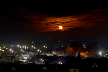 Full moon behind orange clouds over suburban neighborhood with streetlights glowing at night